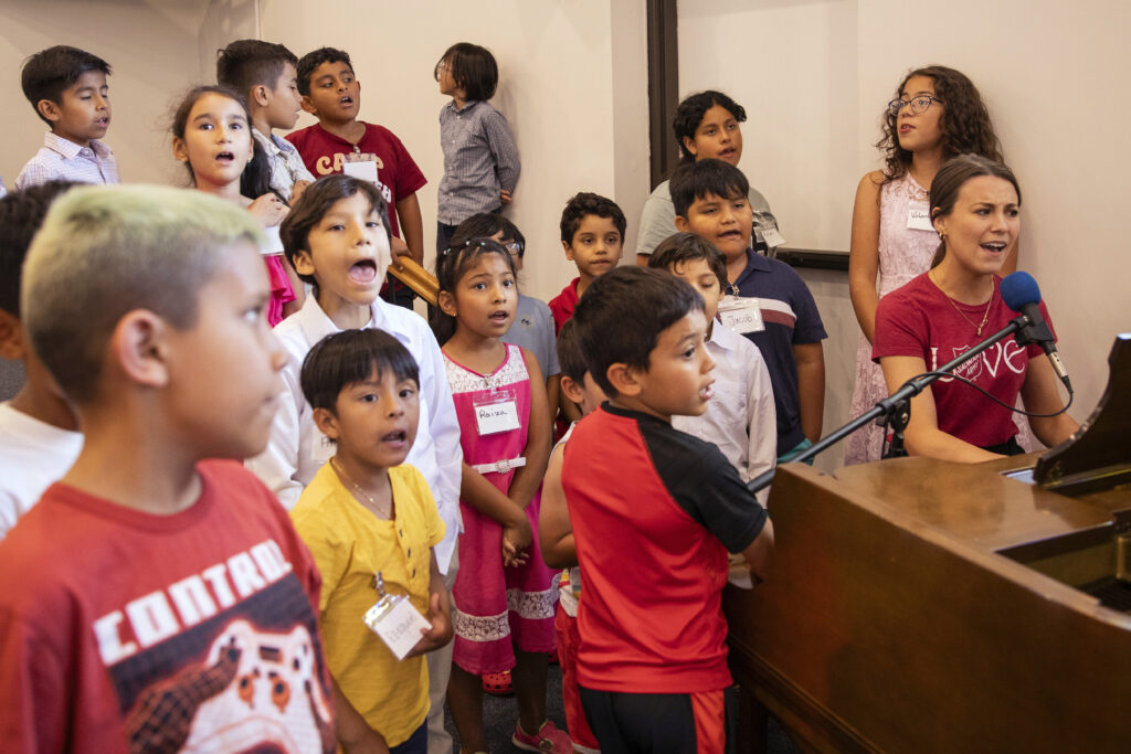 Envoy Emily Betts plays the piano with a group of children.