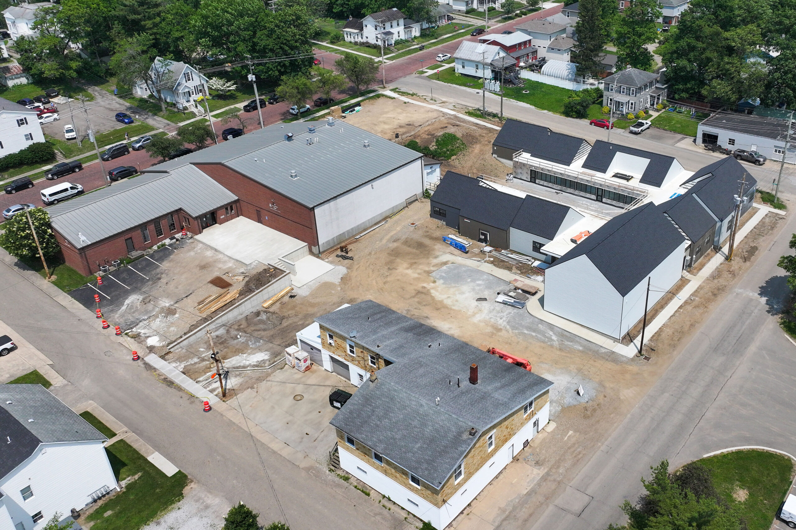 Aerial view of the Salvation Army Learning Lighthouse construction site in June 2025, showing multiple buildings in various stages of development. The site includes a large brick facility and a series of modern, pitched-roof structures arranged around a central courtyard. Surrounding the site are residential homes, tree-lined streets, and construction equipment.